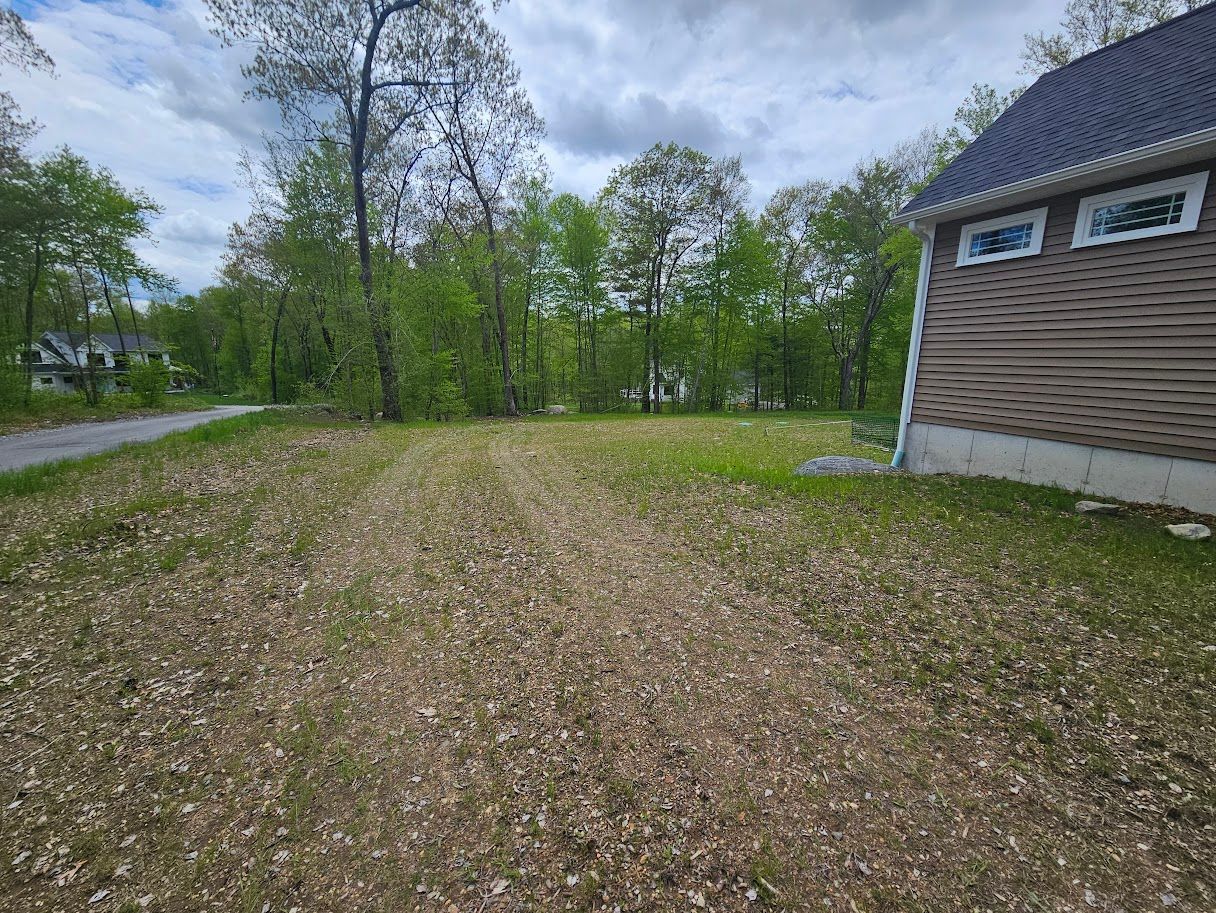 A cleared, brown patch of land bordered by trees and a brown building under a cloudy sky.