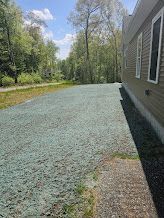 Newly seeded lawn next to a beige house, with trees and a road in the background under a blue sky.