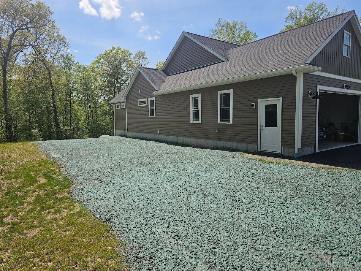 House with gravel-covered lawn; trees and blue sky background. Garage on right side.