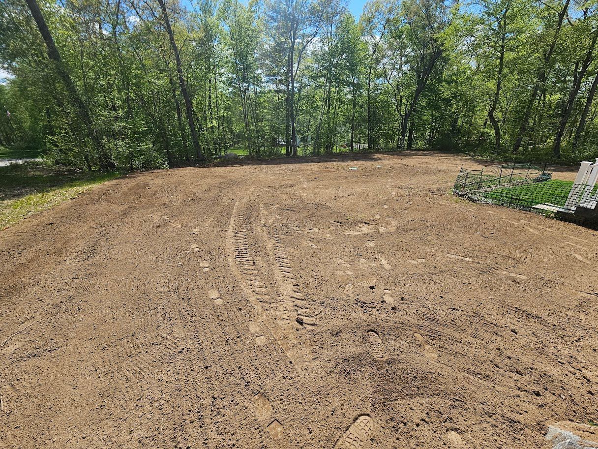 Cleared, tilled dirt area, possibly for landscaping, with trees in the background. Sunny day.