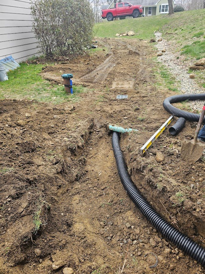 A trench with black drainage pipe being installed in a yard. Soil is piled alongside.