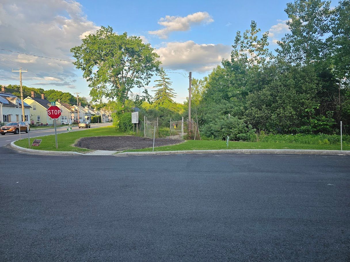 A stop sign at a road's edge. A small landscaped area in a residential neighborhood with trees and a cloudy sky.