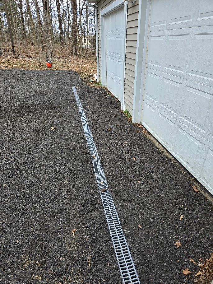 Gravel driveway with a linear drain alongside a white garage.