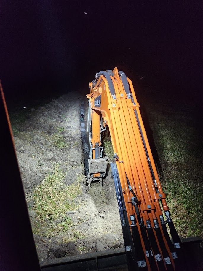 Orange excavator working at night, illuminated by its lights, digging into the dark ground.
