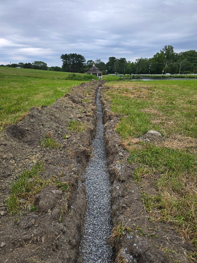 A long trench filled with gray gravel in a grassy field, likely for drainage.