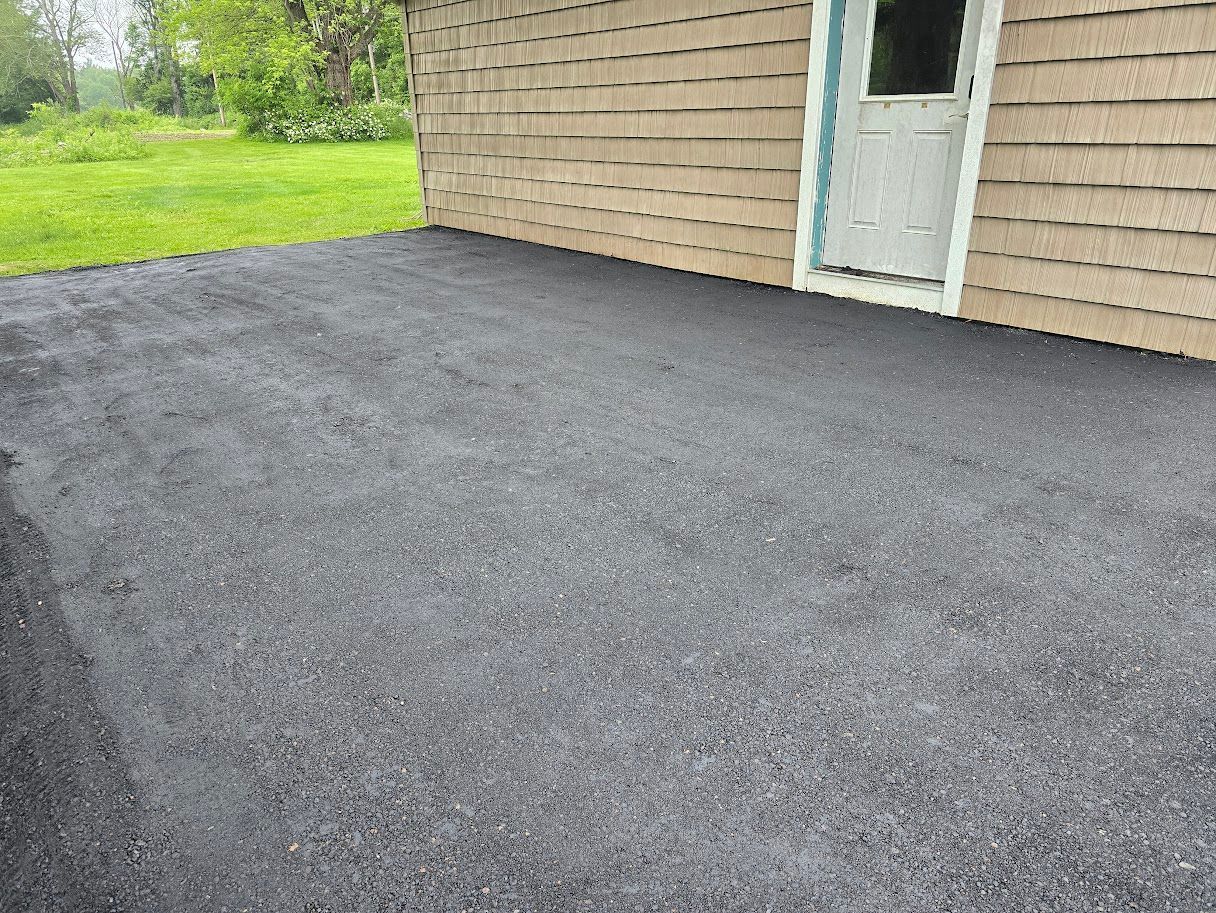 Asphalt paved area next to a light brown building with a white door. Green grass in the background.