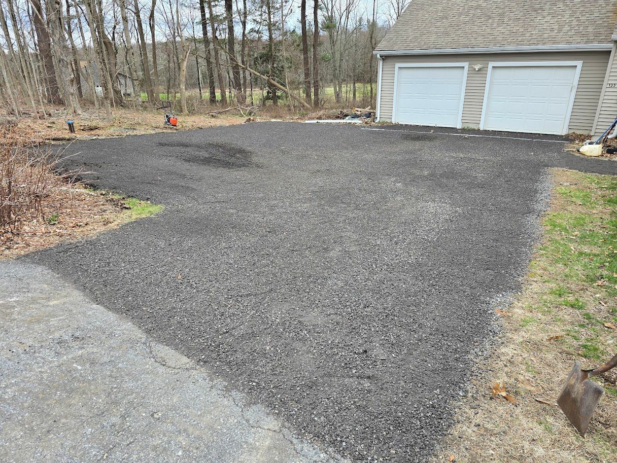 Gravel driveway, next to a grassy area, in front of a garage with white doors.