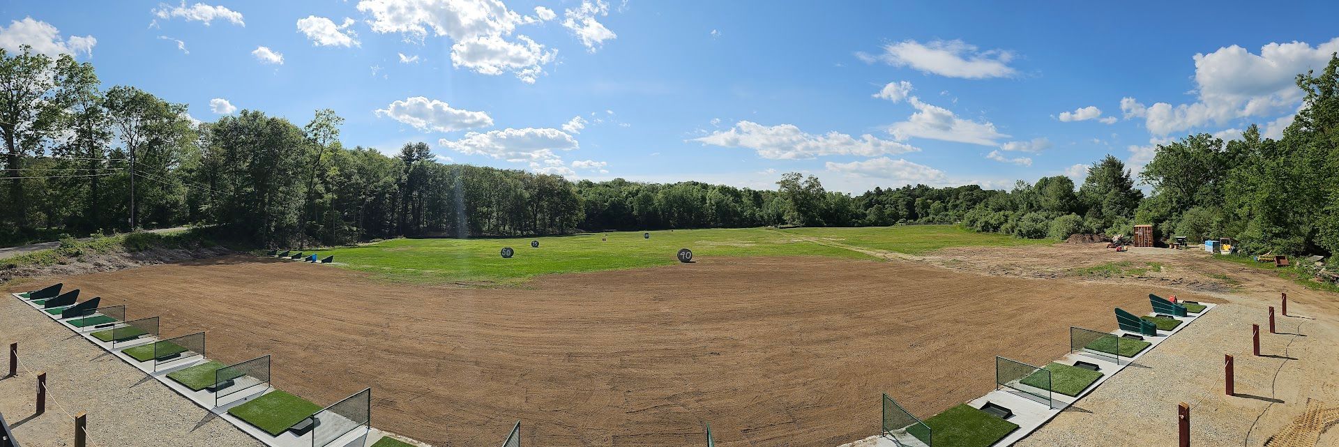 A panoramic view of an outdoor shooting range with marked firing stations in the foreground and a large grass field