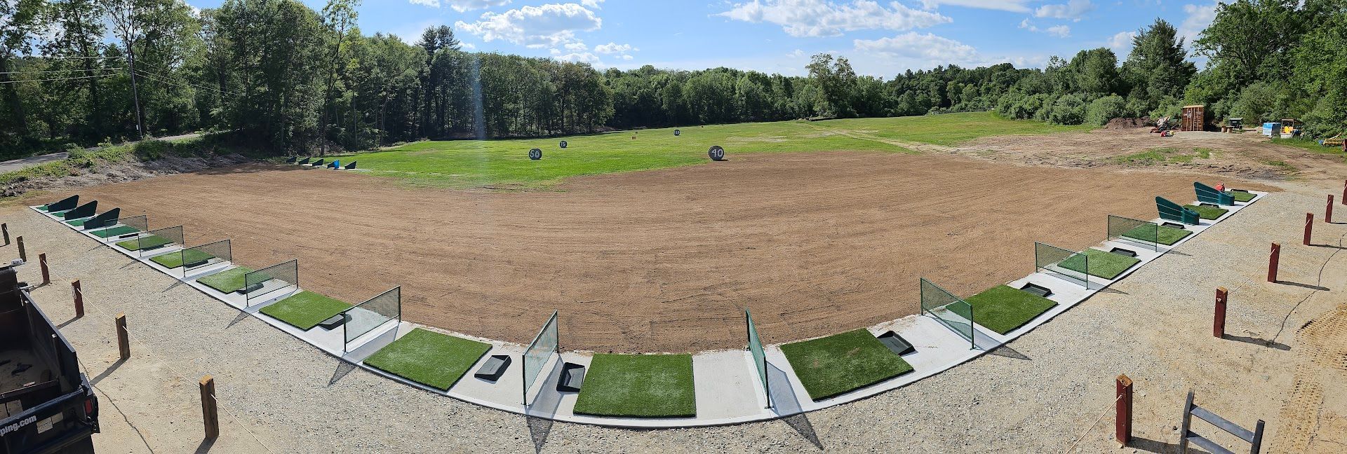 A panoramic view of an outdoor archery range featuring multiple shooting lanes with green mats and dividers facing a field