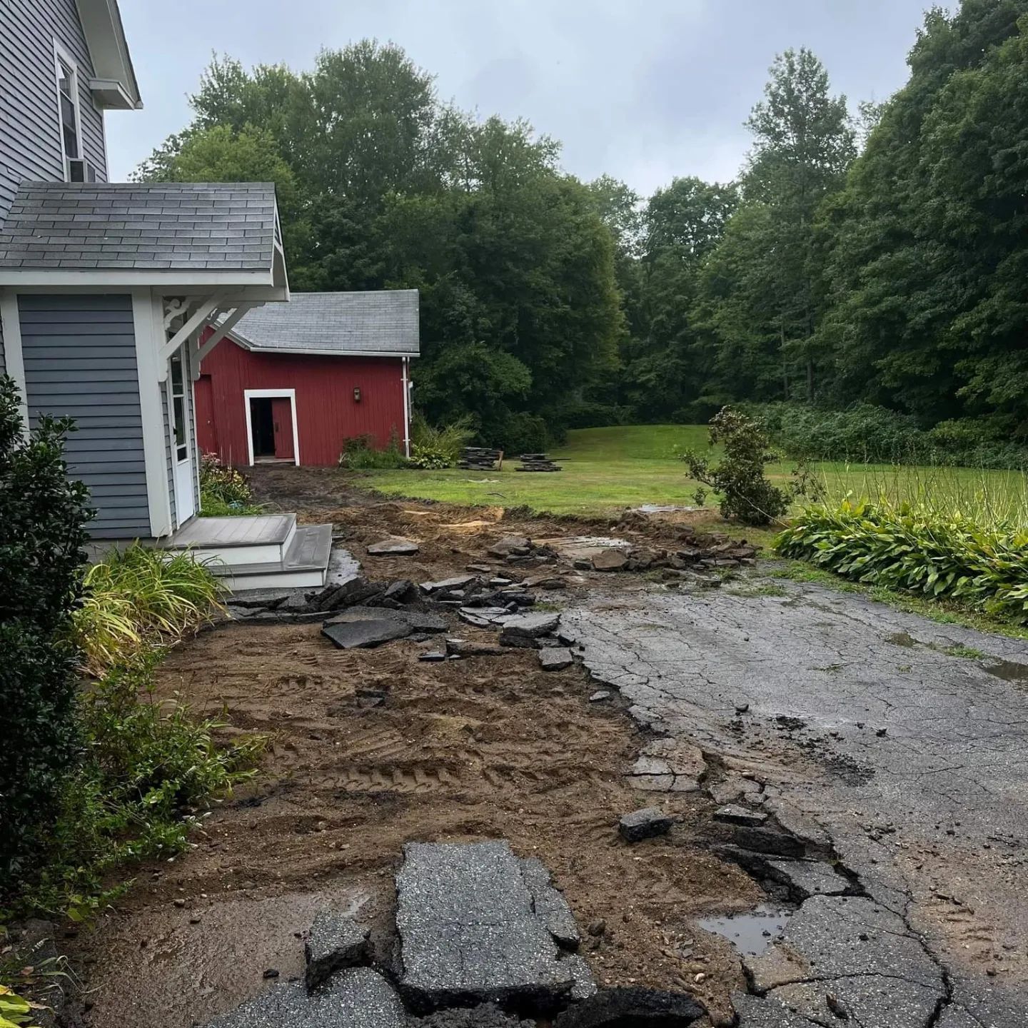 a dirt road leading to a house with a red barn in the background