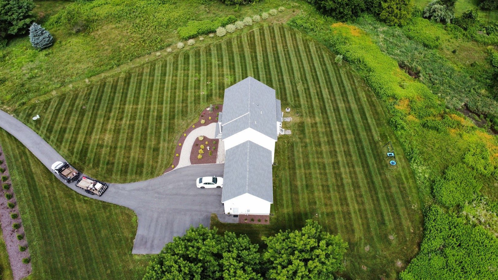 Overhead view of a house with a gray roof and a well-manicured lawn with striped mowing patterns.