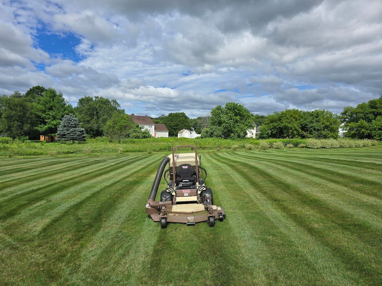 Lawnmower on a large lawn, mowing striped pattern under a cloudy sky.