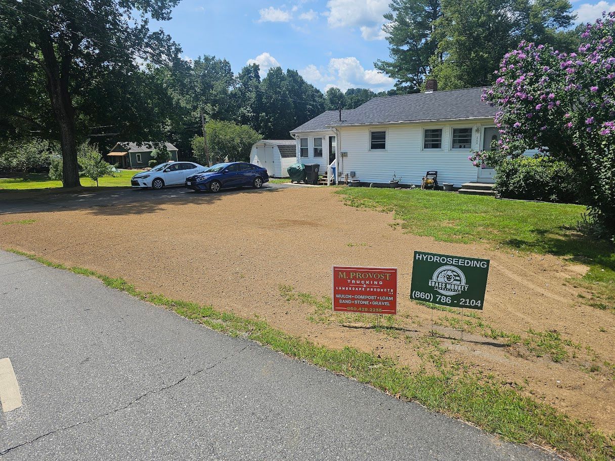 A gravel driveway leads to a white one-story building, with two yard signs in the foreground and parked cars behind