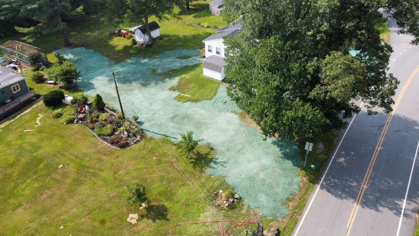 An aerial view of a yard featuring a large area of green spray-on mulch used for erosion control near a road and house