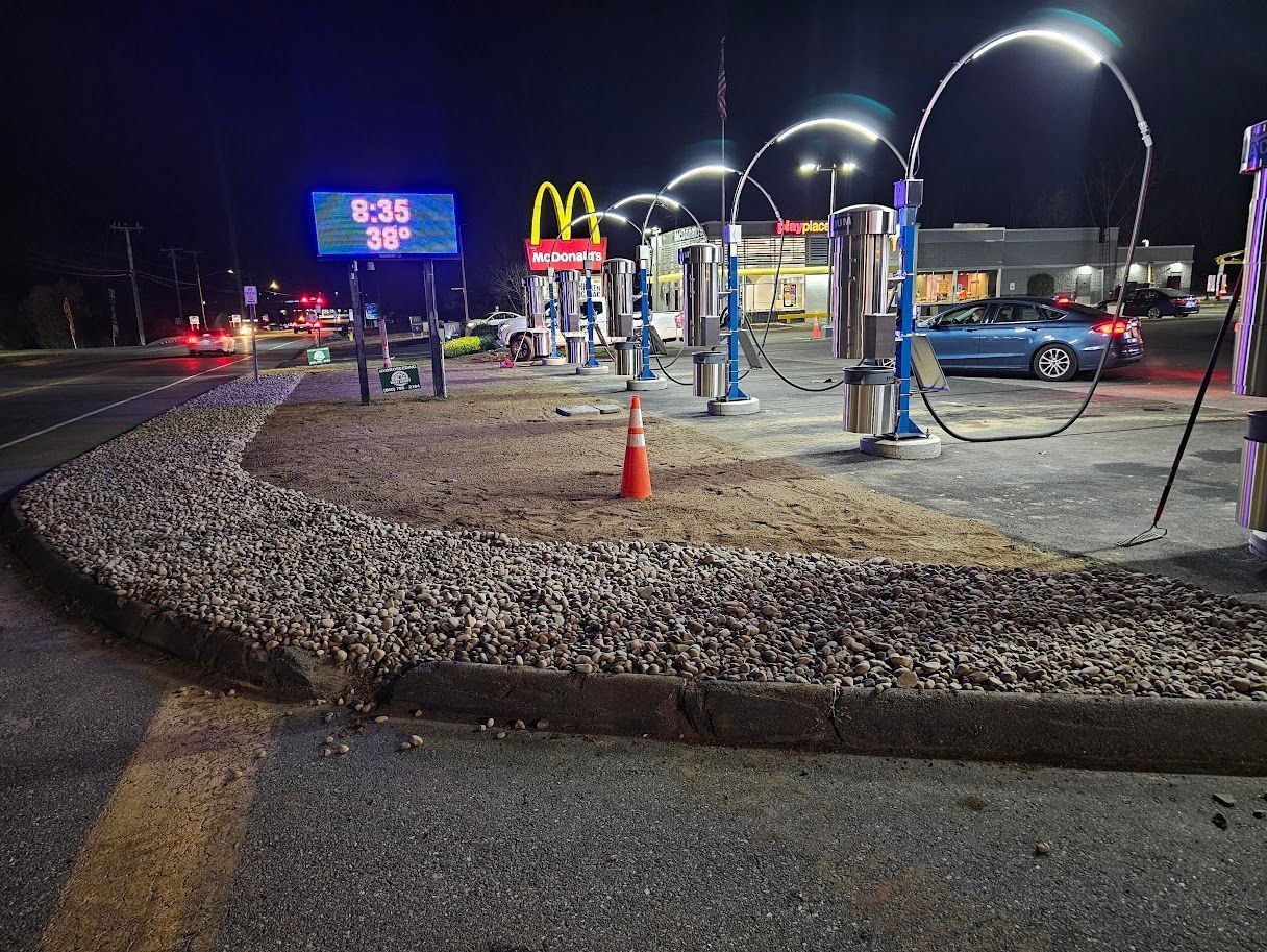 A McDonald’s restaurant with illuminated drive-thru arches at night, adjacent to a road with a digital time and temp sign