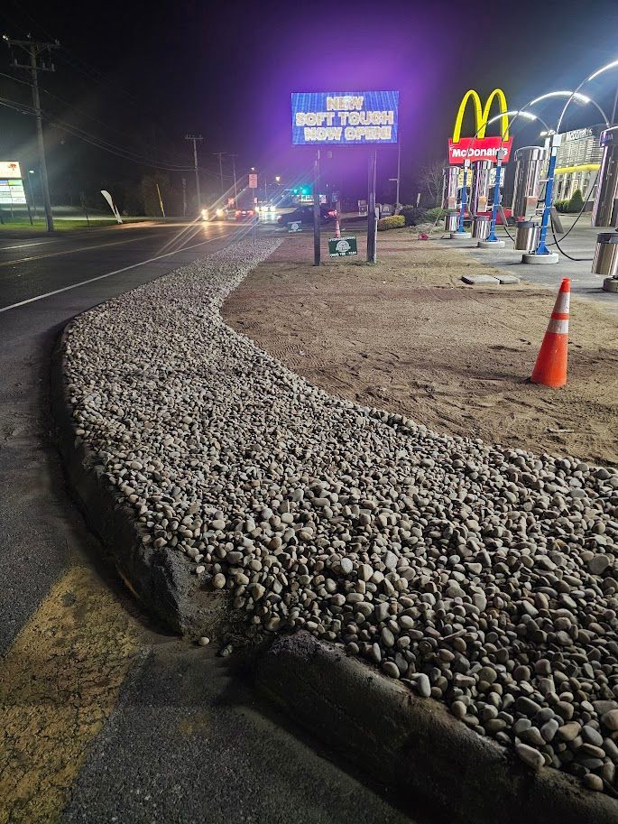 A rock-filled curb borders a dirt area with an orange traffic cone
