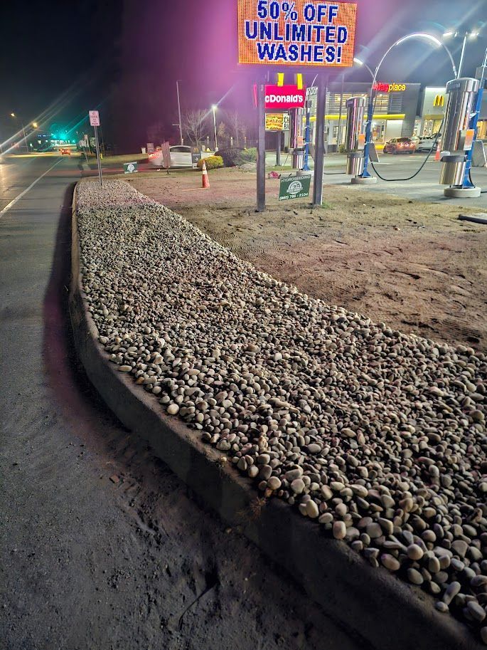 A gravel-filled garden bed lines a paved lot at night