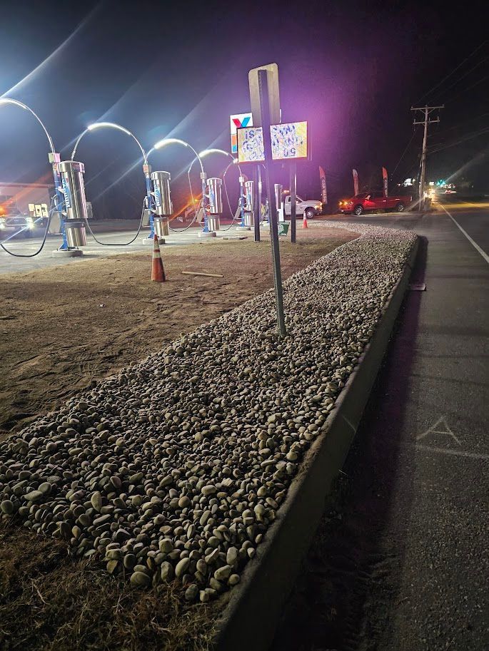 Night view of a car wash lot featuring illuminated archways and a gravel median bordering a paved road