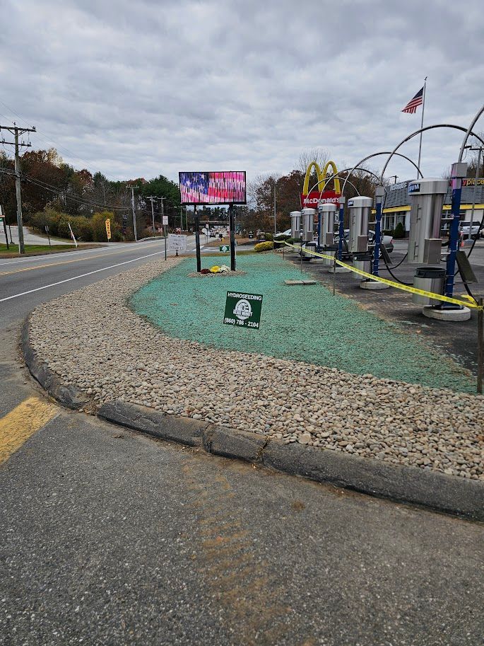 A car wash with a digital American flag sign and a small square sign in the green landscaped area by the roadside