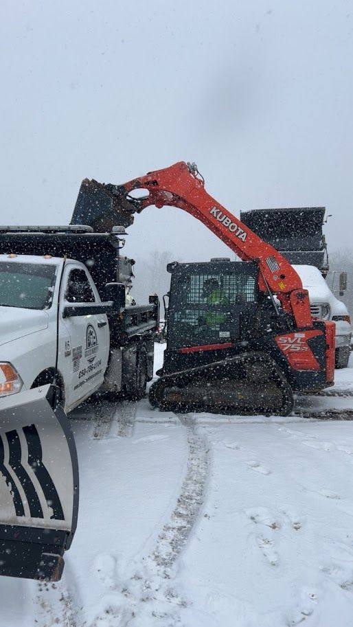Orange Kubota track loader loading a white truck with black material in a snowy setting.