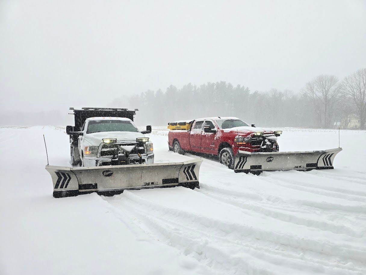 Two snowplow trucks clearing snow in a snowy field. One white, one red.