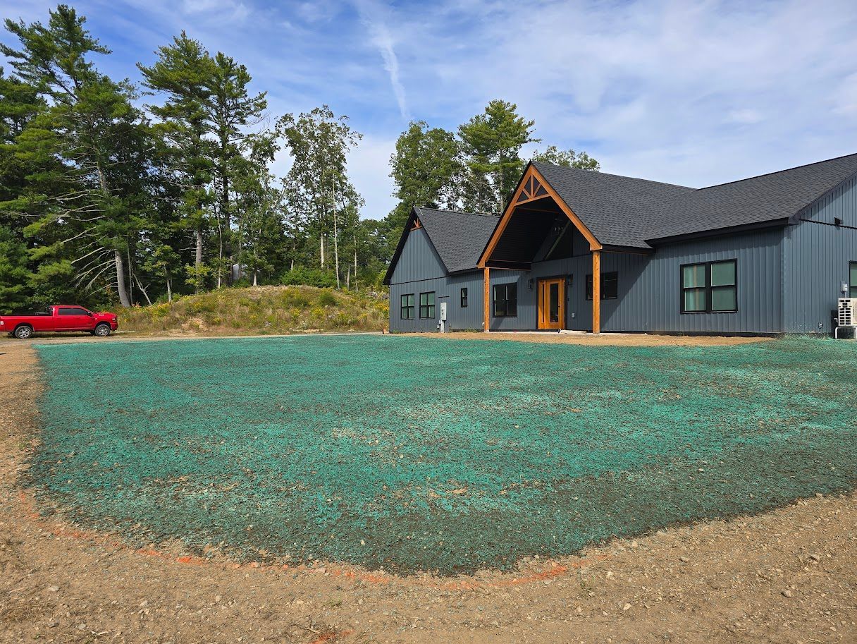 A blue house with a gray roof and a green seeded lawn on a sunny day with a red truck.