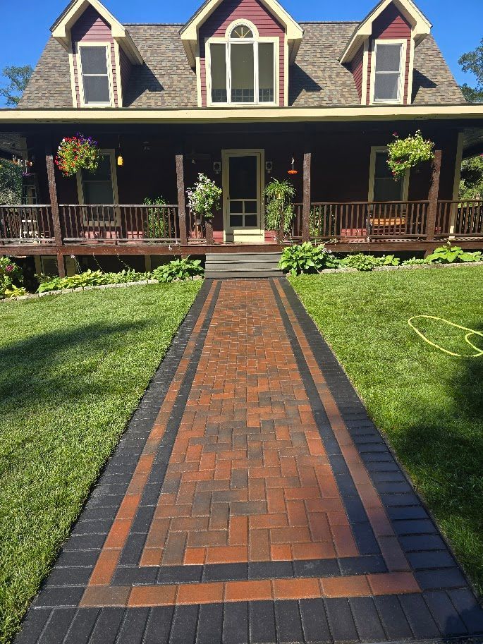 Brick walkway leading to a red house with a porch. Green lawn surrounds the path.