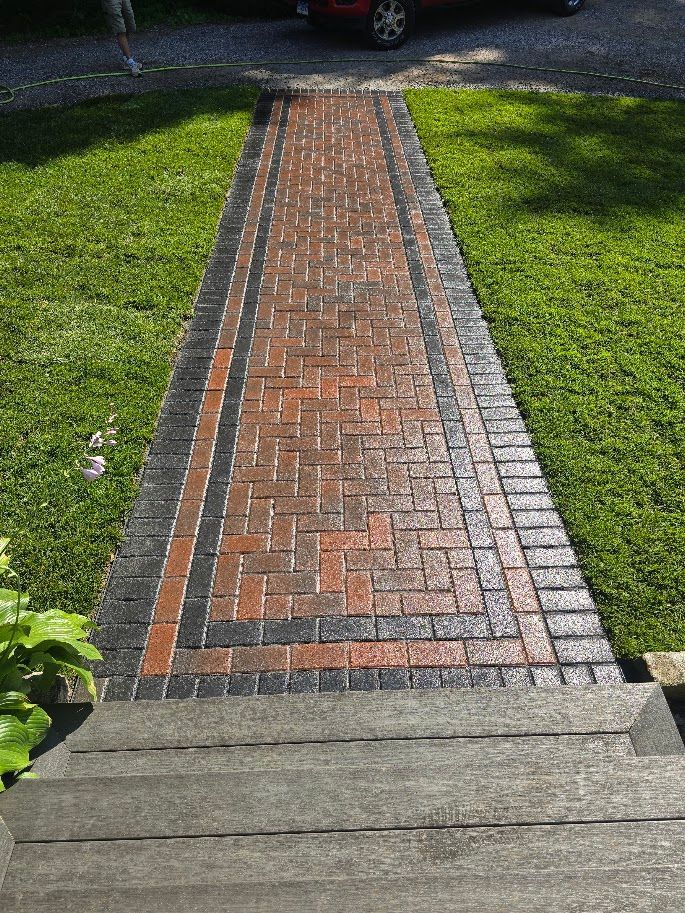 Brick walkway with brick and dark border, leading through green grass.