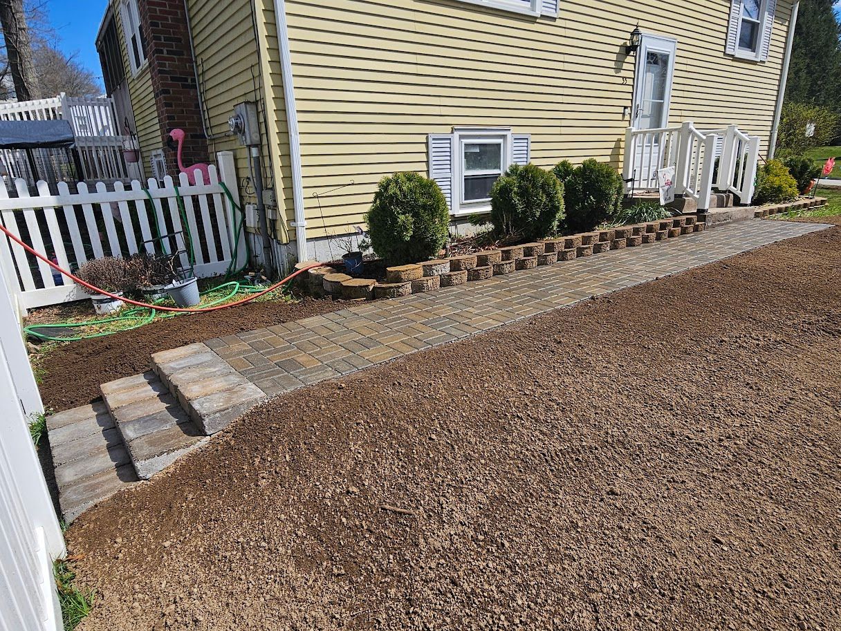 Stone steps lead up to a house with a gravel path, a retaining wall, and shrubs.