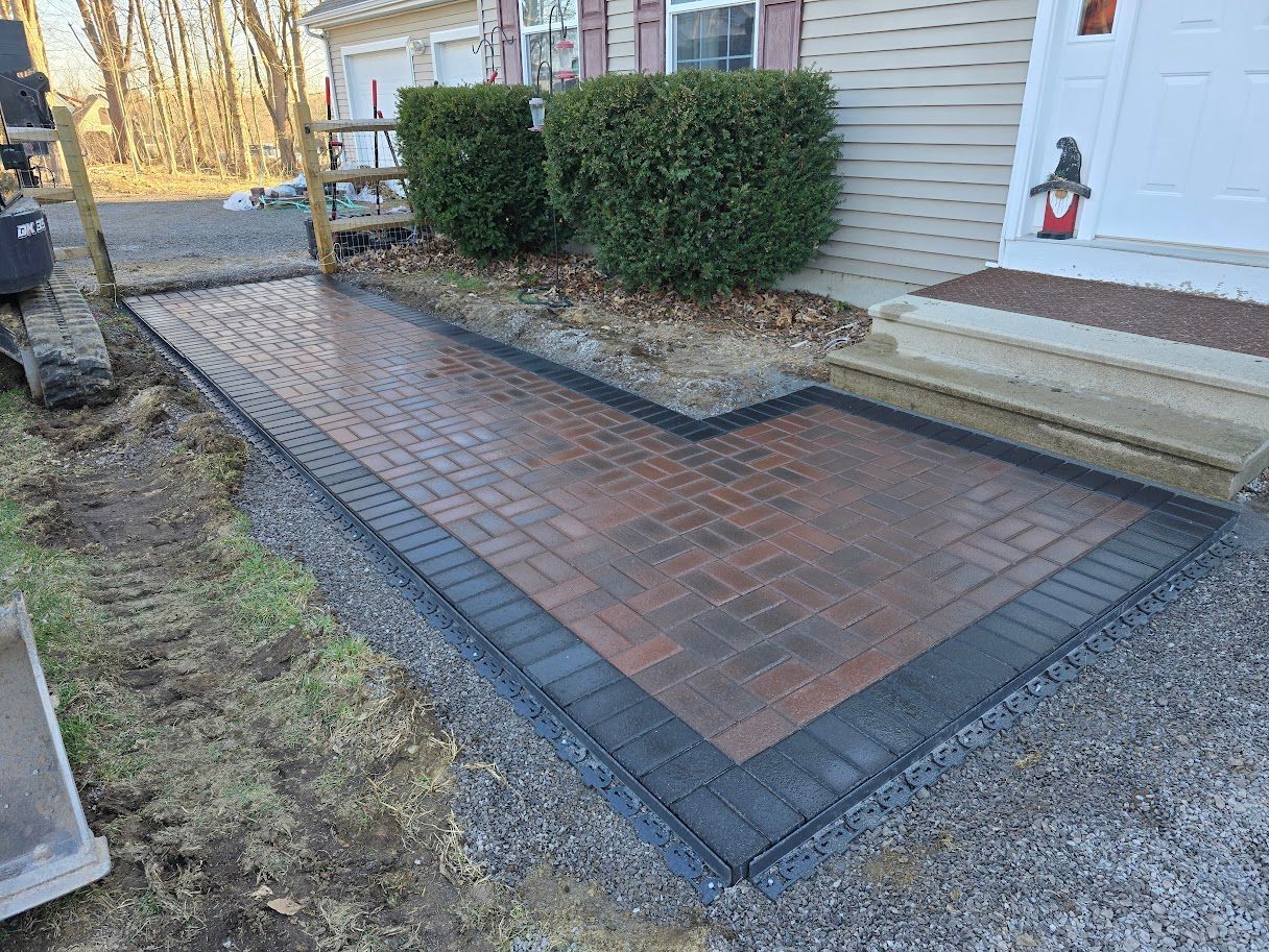 Brick walkway leading to a house entrance with shrubbery and a dark border, set in gravel.