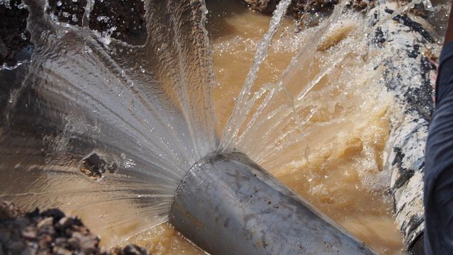 Water spraying forcefully from a broken pipe into muddy brown water