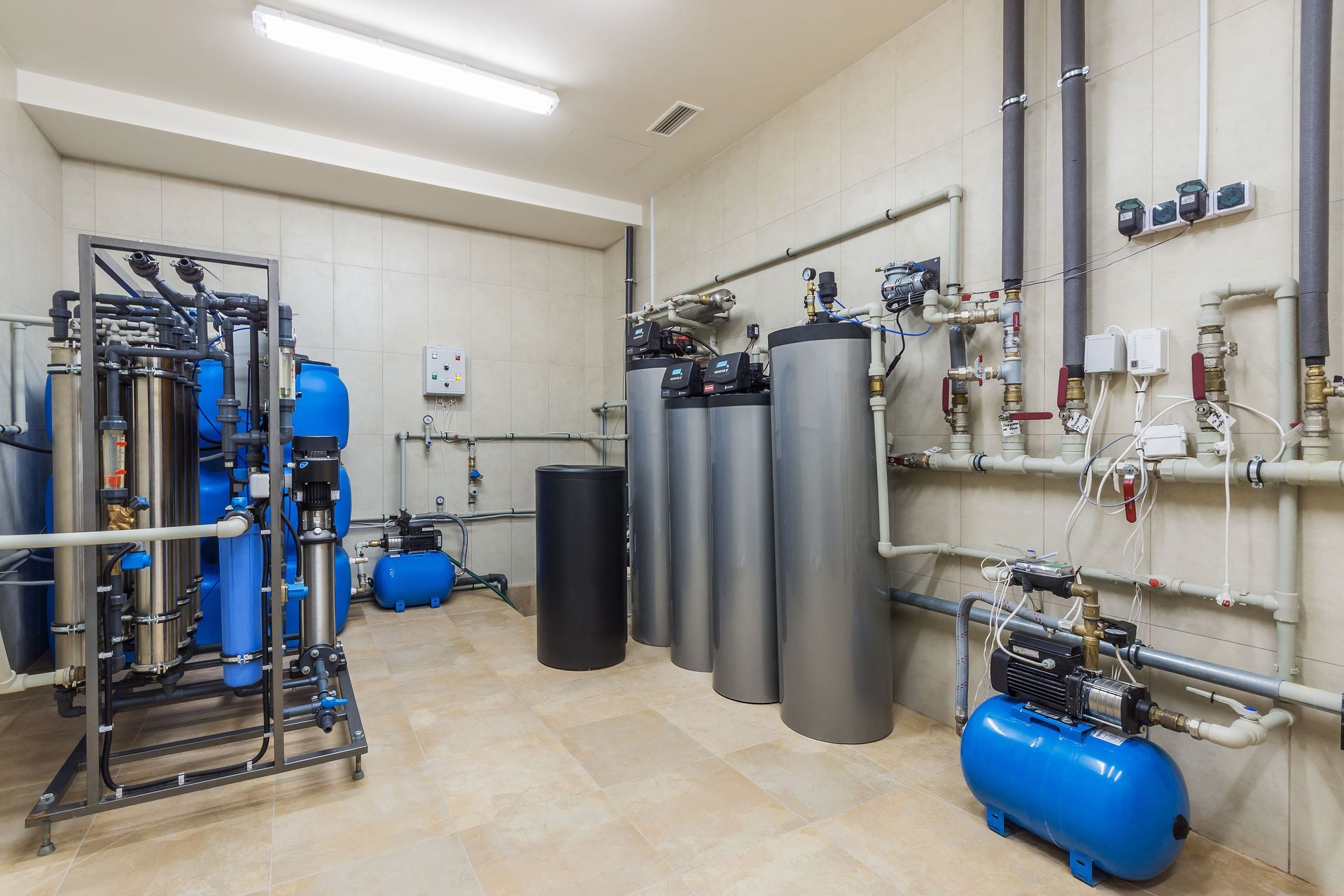 Water treatment system in a utility room with blue and gray equipment. Pipes run along the walls.