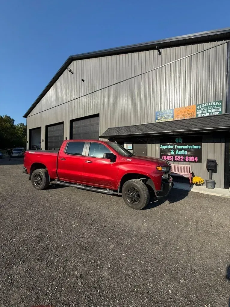 Red pickup truck parked in front of a gray metal building with black garage doors and a sign.