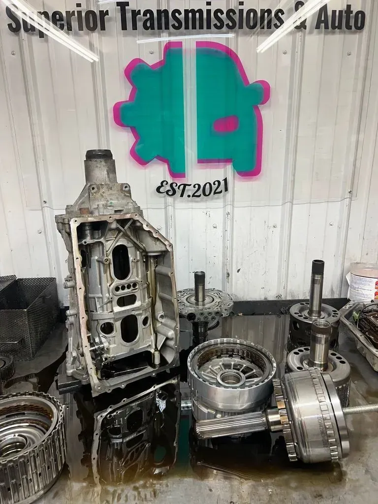 Disassembled car transmission parts on a workbench in a mechanic shop with logo reading "Superior Transmissions & Auto."