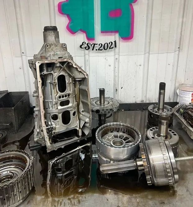 Disassembled car transmission parts on a workbench in a mechanic shop with logo reading "Superior Transmissions & Auto."