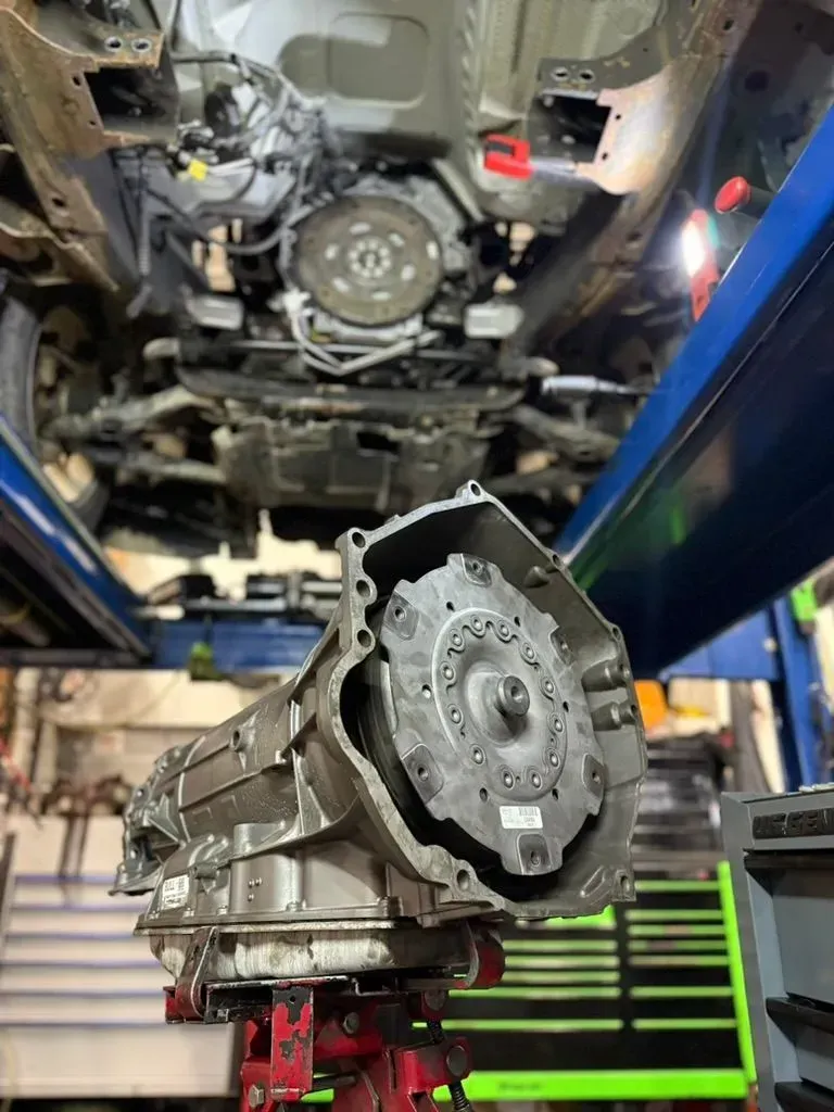 A car's underside with a removed transmission on a lift in a garage.