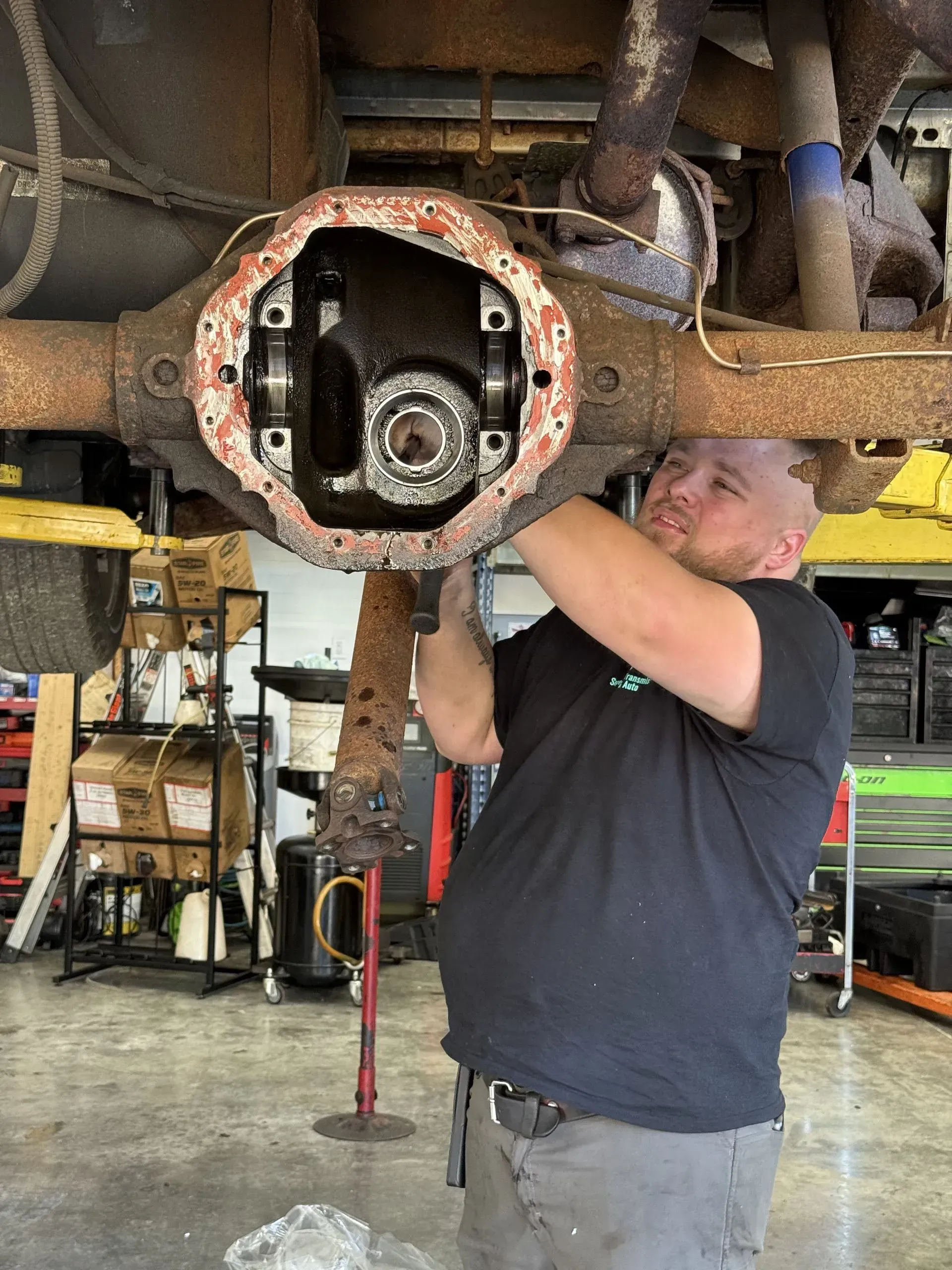 Mechanic working on the open differential of a rusty vehicle. Shop interior.