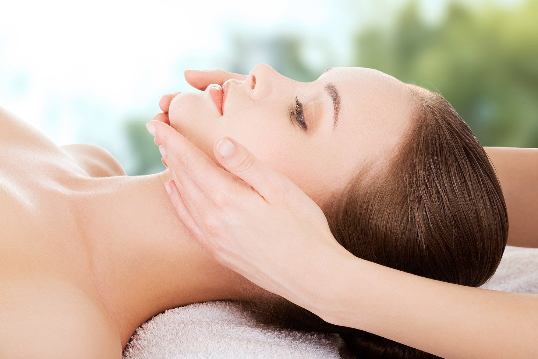 Woman receiving facial massage with hands on her face, eyes closed.