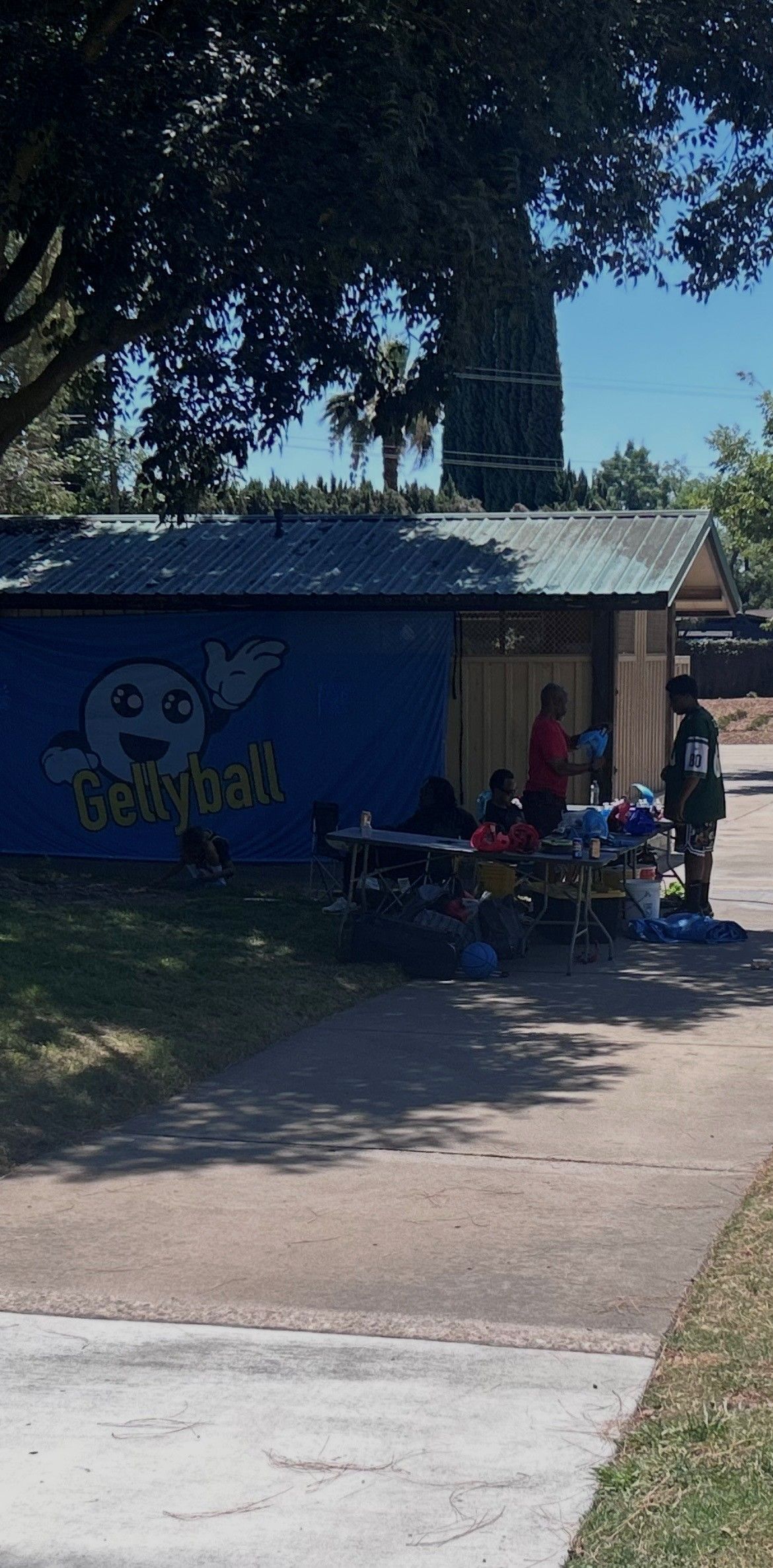Small blue roadside building with people sitting in the shade under trees