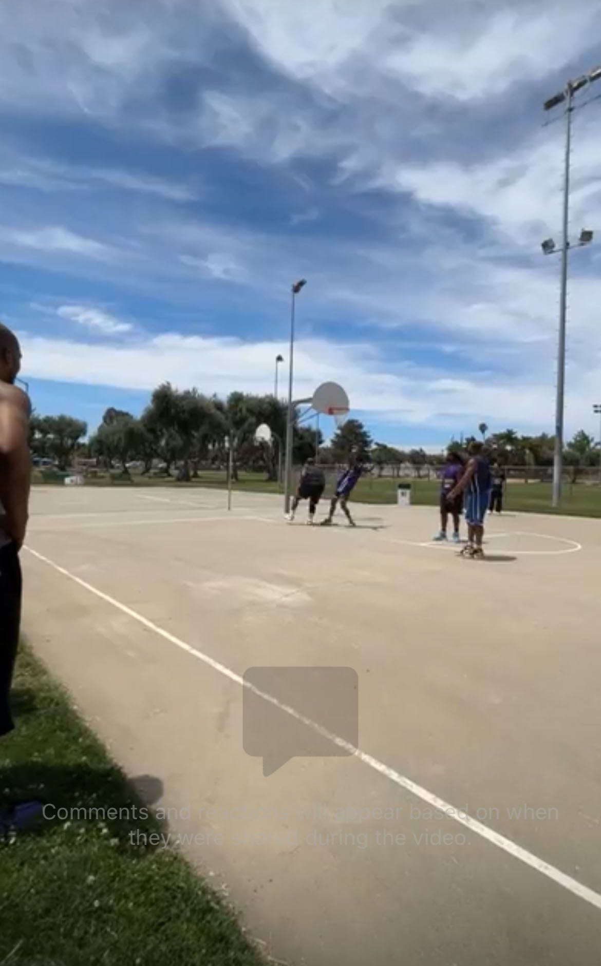 A group of people is playing basketball on a court in a park.