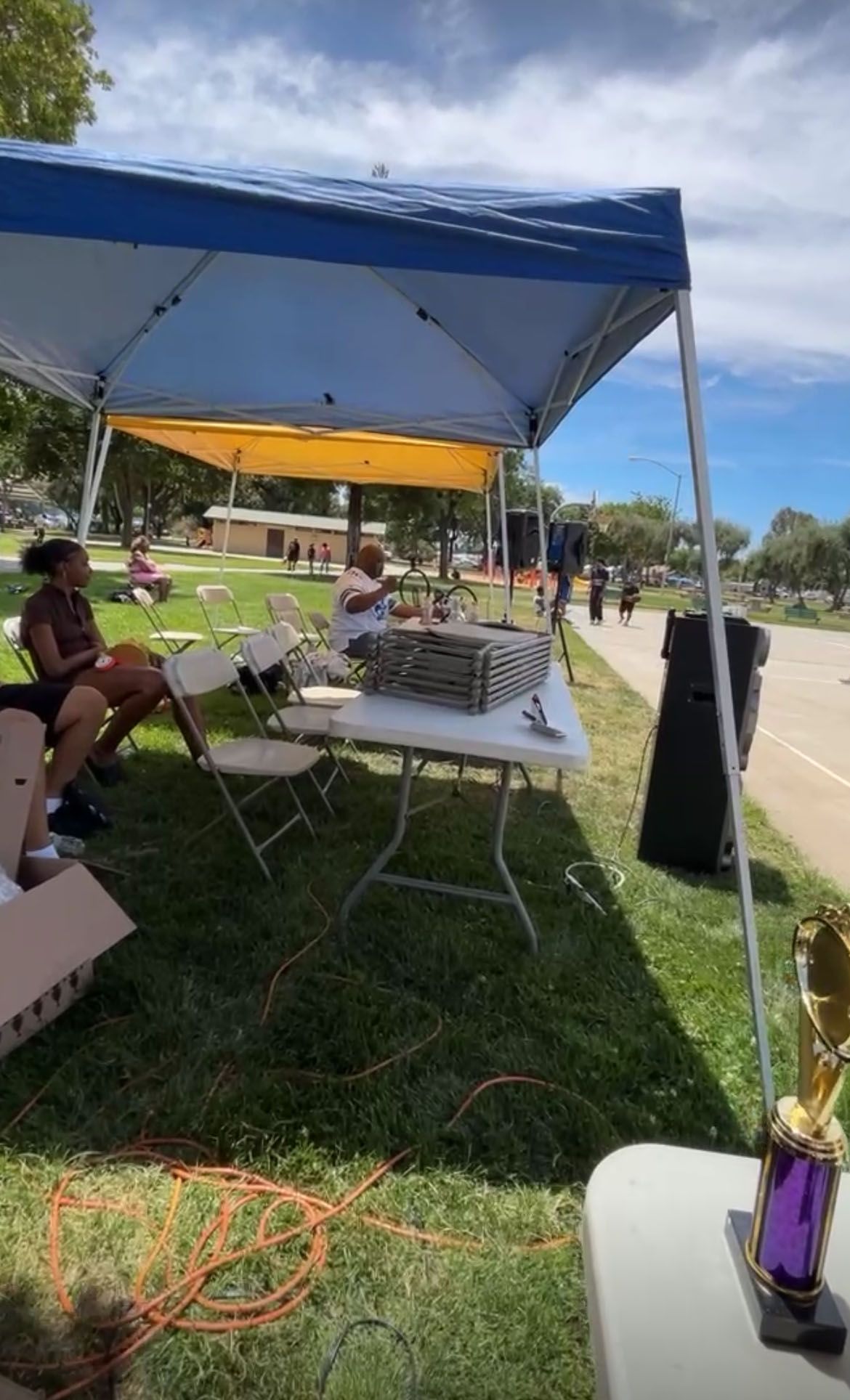A group of people is sitting under a tent in a park.
