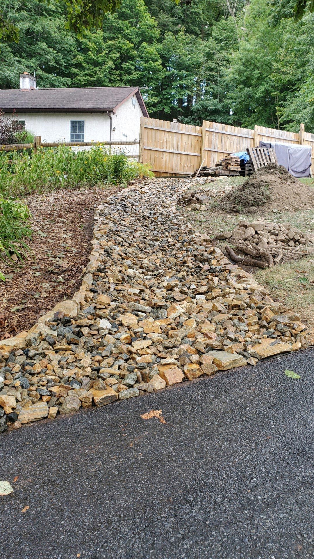 A pile of rocks is sitting on the side of a road in front of a house.