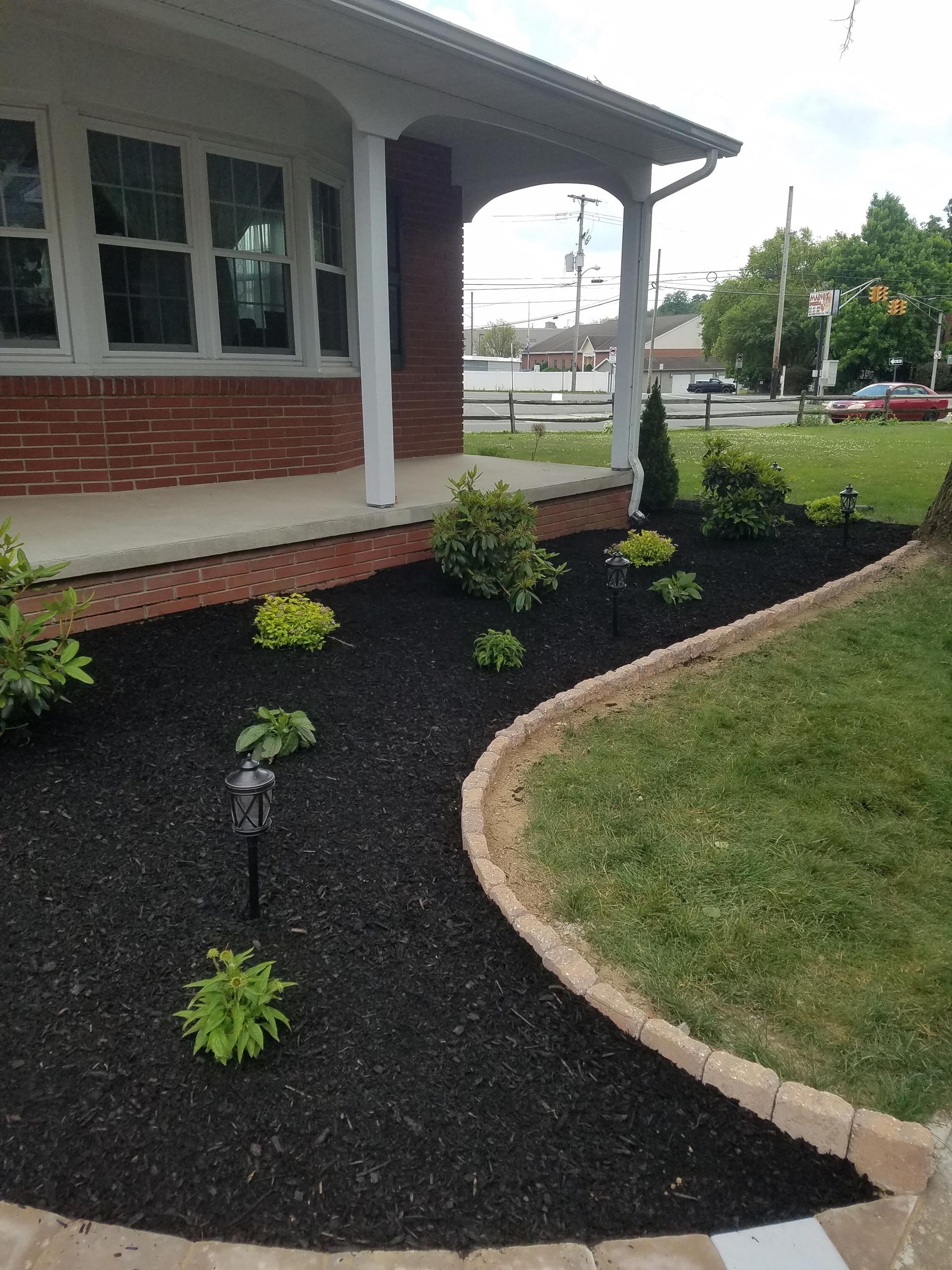 A house with a lush green lawn and a black mulch garden in front of it.