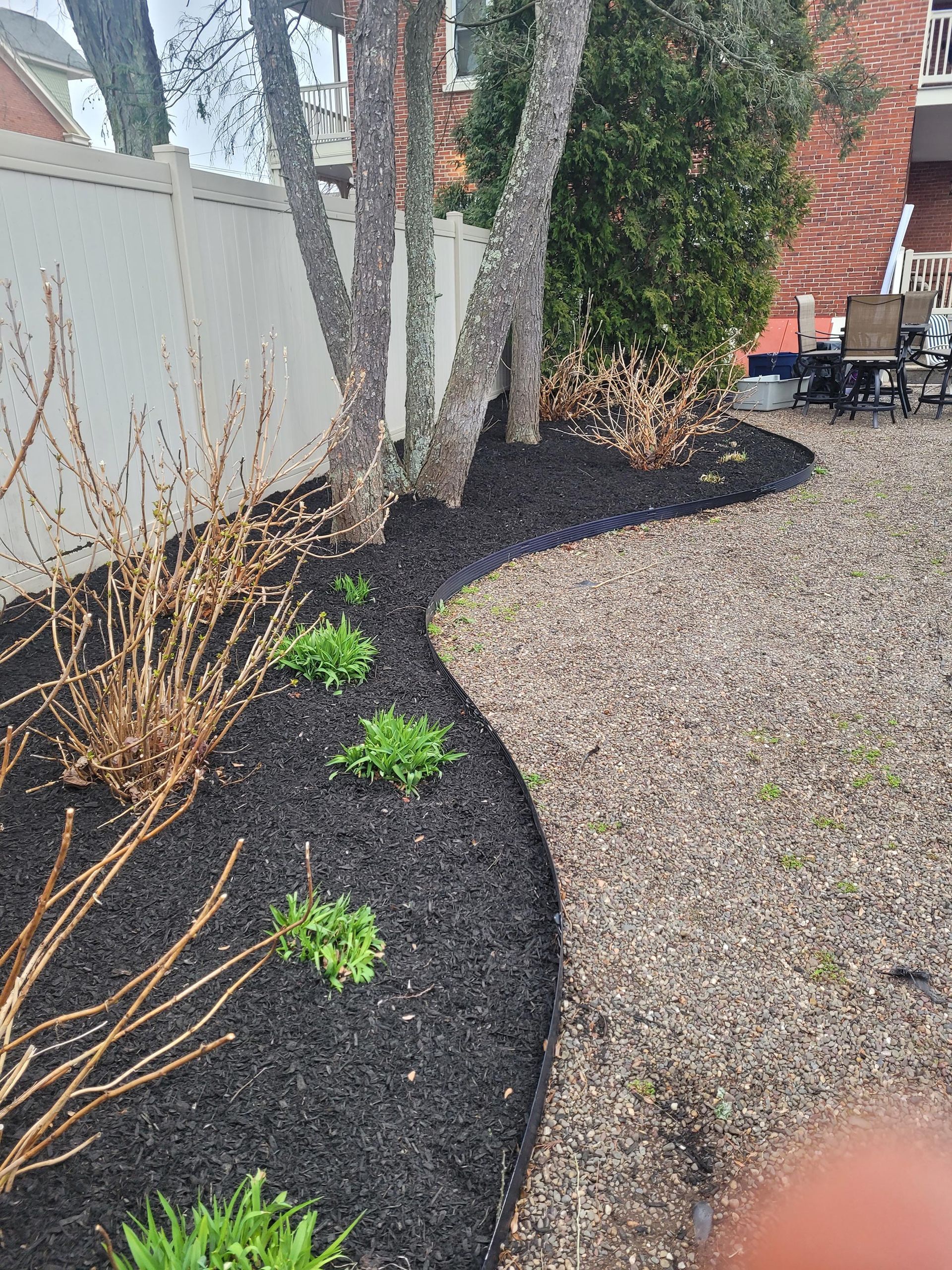 A backyard with a fence , a table and chairs , and a few trees.