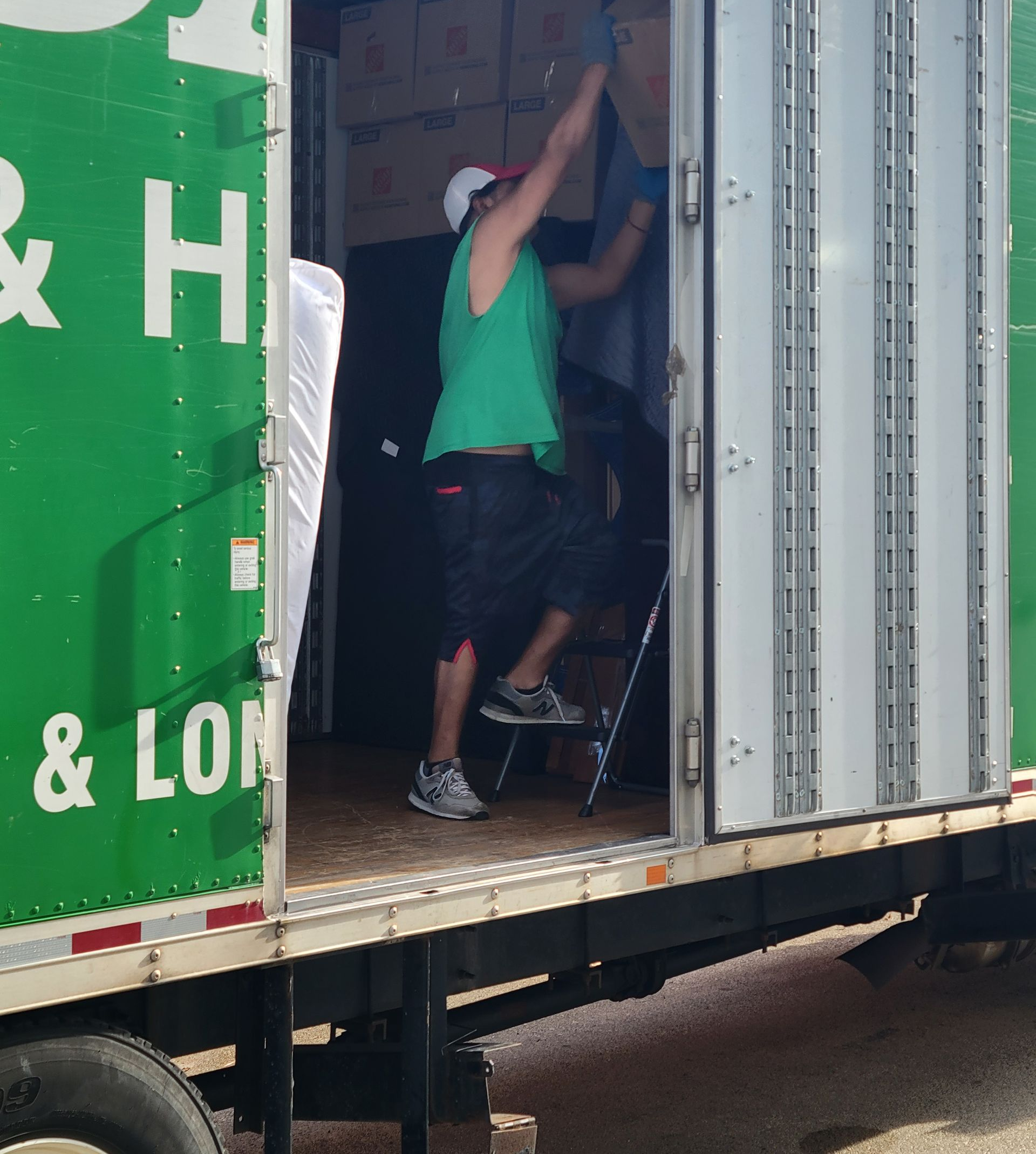 Man loading boxes into a truck; green and white exterior. He's wearing a green shirt and a hat.