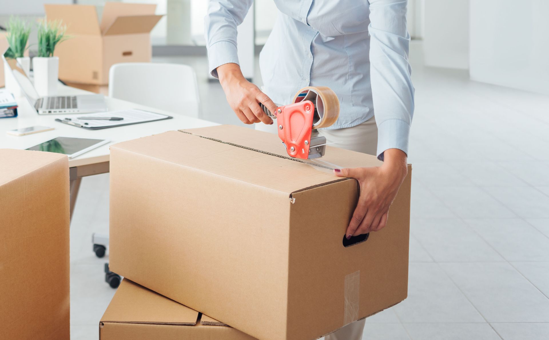 Woman taping a cardboard box in an office setting, preparing for a move.