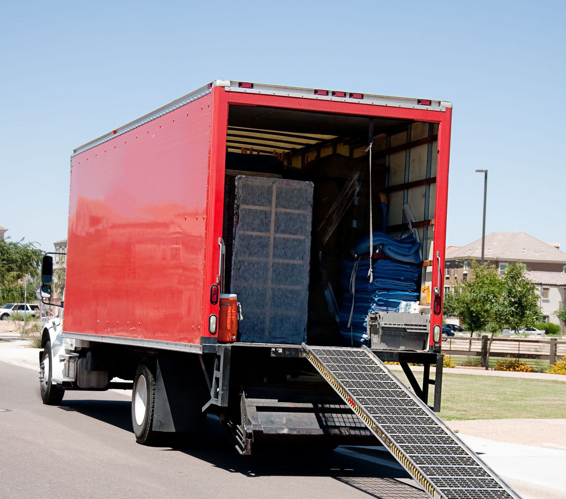Red moving truck with ramp down, loaded with furniture in a residential setting.