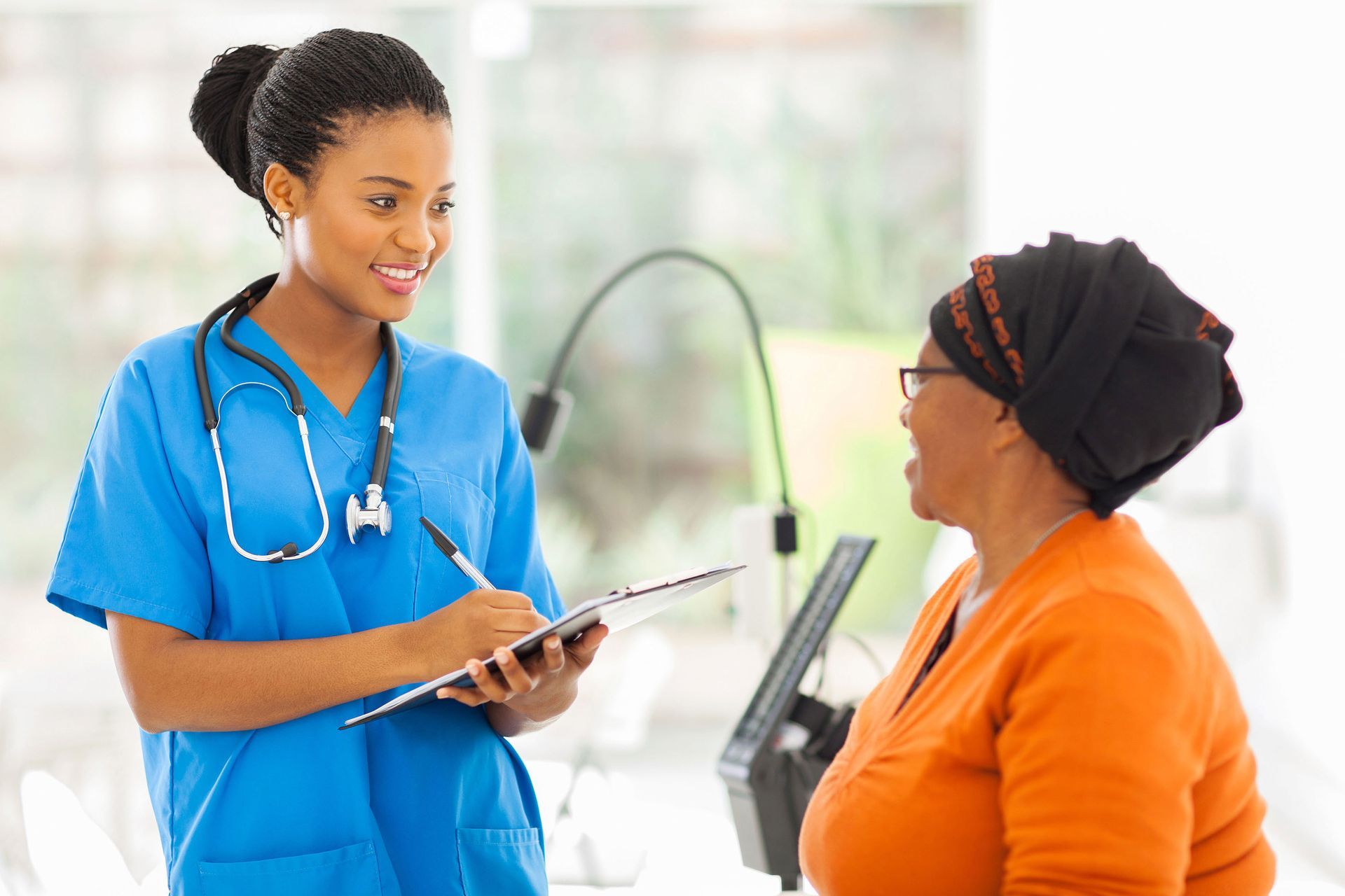 A nurse is talking to a woman while holding a clipboard.