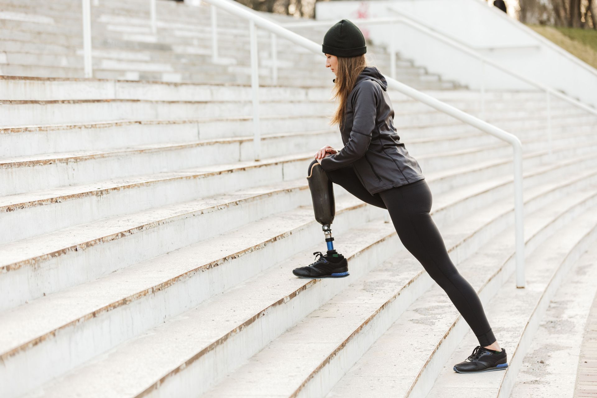 A woman with a prosthetic leg is stretching her legs on a set of stairs.