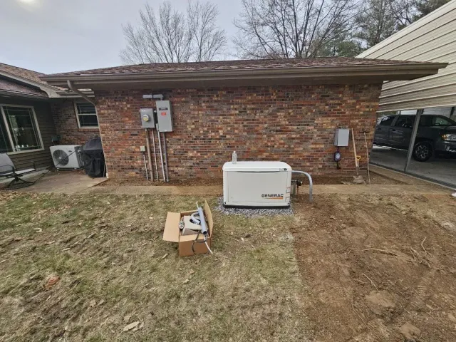 Backyard view of a brick house wall with a white utility unit, lawn, and a cardboard box.